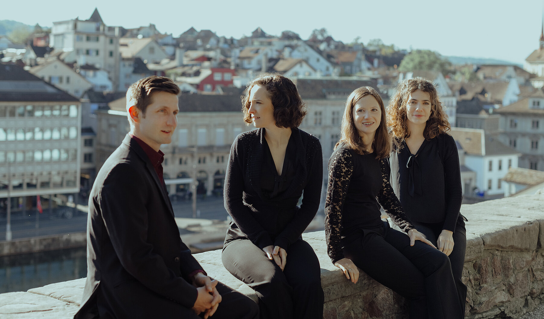 Das Belenus Quartett sitzt auf einer Steinmauer über der Zürcher Altstadt im warmen Abendlicht